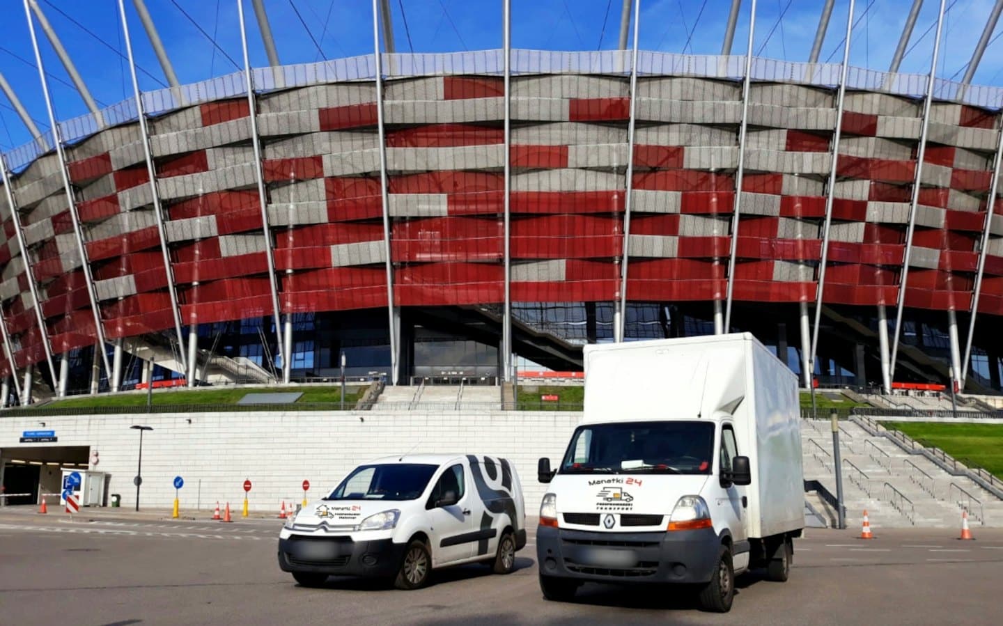 Dvě dodávky zaparkované před stadionem.